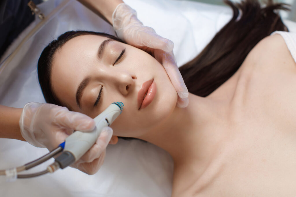 Woman lying down on table in spa facility undergoing a HydraFacial treatment.