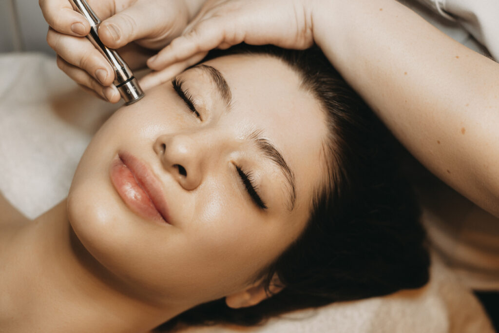 Woman lying down on table in a spa facility having a microdermabrasion treatment on her face.