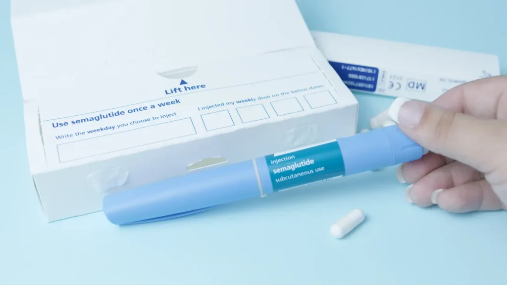 Hand holding a blue semaglutide injection pen beside an open medication box and white capsule.