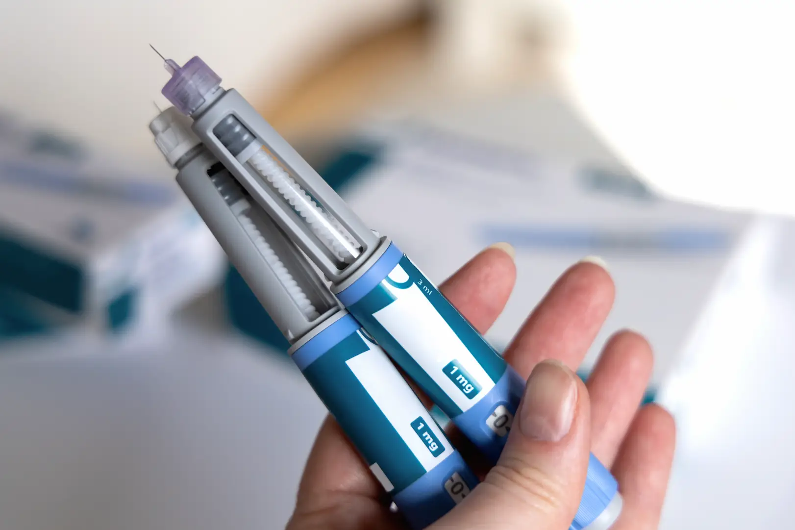 Hand holding two blue injection pens with exposed needles and 1 mg labels.